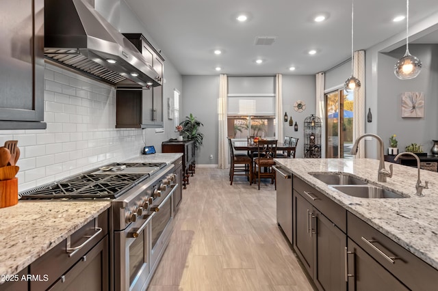 kitchen with sink, light stone counters, decorative light fixtures, ventilation hood, and appliances with stainless steel finishes