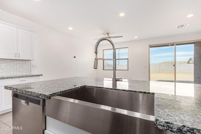 kitchen with stone countertops, visible vents, dishwasher, backsplash, and a sink