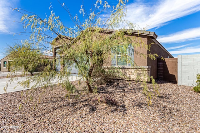 view of side of home featuring stone siding, fence, and stucco siding