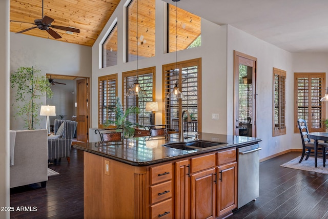 kitchen featuring a sink, dark stone counters, dishwasher, an island with sink, and a ceiling fan