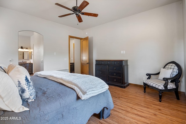bedroom featuring wood finished floors, a ceiling fan, baseboards, arched walkways, and ensuite bath