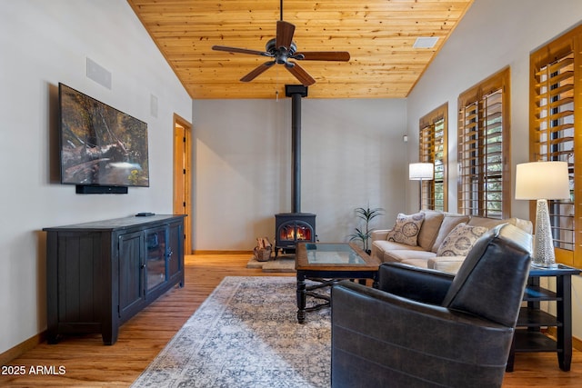 living room featuring vaulted ceiling, a wood stove, baseboards, and wooden ceiling