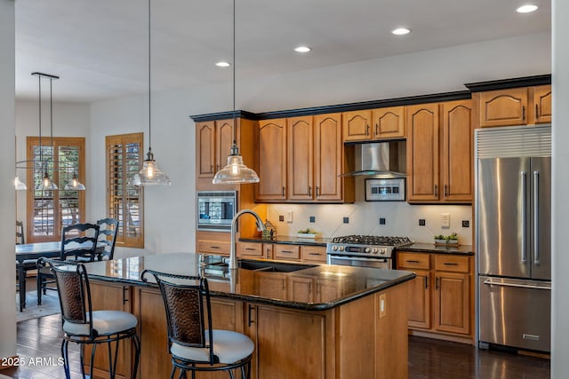 kitchen with a sink, stainless steel appliances, a kitchen island with sink, exhaust hood, and tasteful backsplash