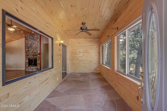 unfurnished sunroom with a stone fireplace, ceiling fan, wood ceiling, and lofted ceiling