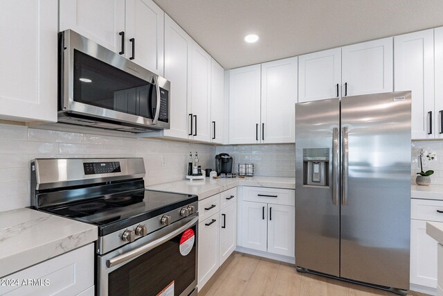 kitchen featuring stainless steel appliances, white cabinets, light wood-type flooring, and tasteful backsplash