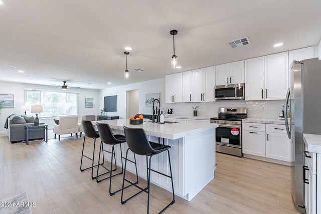 kitchen featuring hanging light fixtures, light hardwood / wood-style floors, a kitchen island with sink, and stainless steel appliances