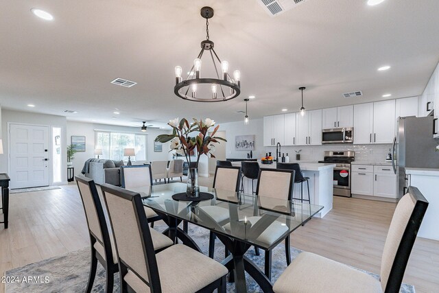 dining area with sink, ceiling fan with notable chandelier, and light hardwood / wood-style floors