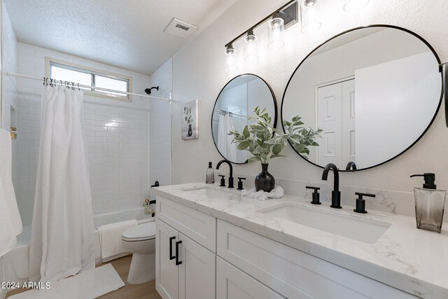 full bathroom with a textured ceiling, vanity, toilet, and shower / bath combo with shower curtain