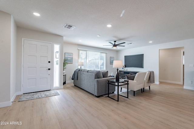 living room with a textured ceiling, ceiling fan, and light hardwood / wood-style flooring