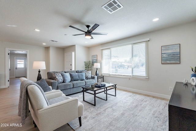 living room with light hardwood / wood-style floors, ceiling fan, and a textured ceiling