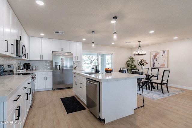 kitchen with an island with sink, stainless steel appliances, pendant lighting, and light wood-type flooring