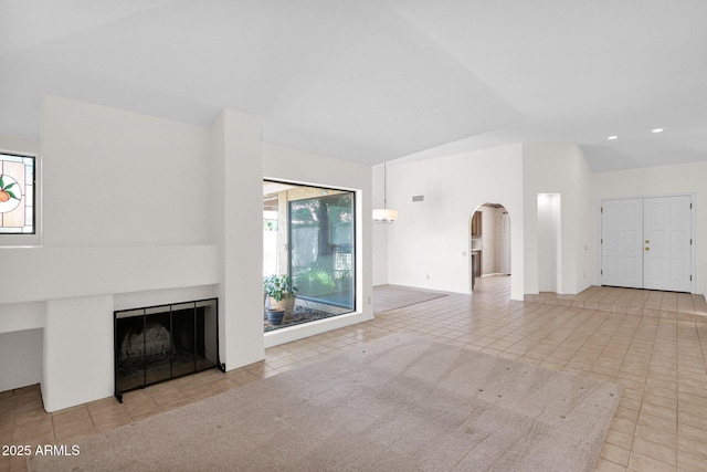 9797 N 100th Pl, Scottsdale, AZ 85258 - unfurnished living room featuring arched walkways, tile patterned flooring, a tiled fireplace, vaulted ceiling, and recessed lighting