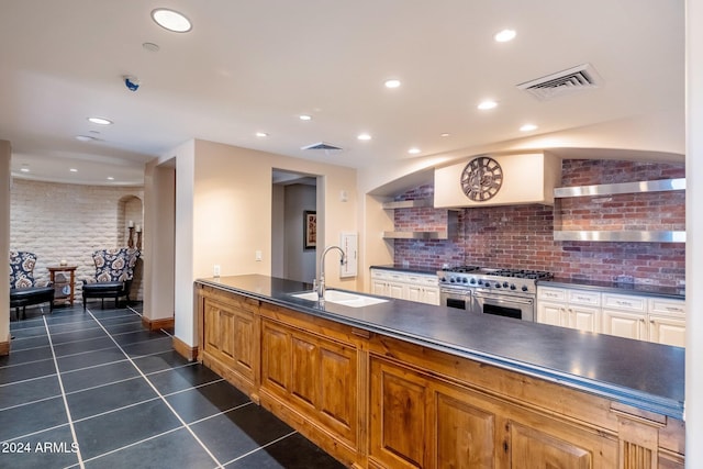 kitchen featuring backsplash, high end stove, extractor fan, sink, and dark tile patterned flooring