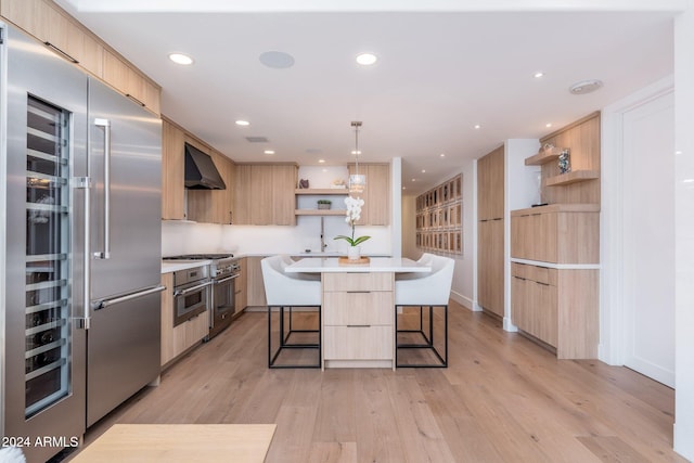 kitchen featuring high quality appliances, wall chimney range hood, hanging light fixtures, a kitchen island, and a kitchen bar