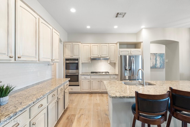 kitchen with sink, light stone counters, appliances with stainless steel finishes, a kitchen breakfast bar, and light hardwood / wood-style floors