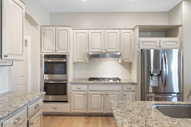 kitchen featuring tasteful backsplash, light stone countertops, stainless steel appliances, and light hardwood / wood-style floors