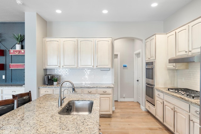 kitchen featuring appliances with stainless steel finishes, tasteful backsplash, sink, light stone counters, and light hardwood / wood-style floors