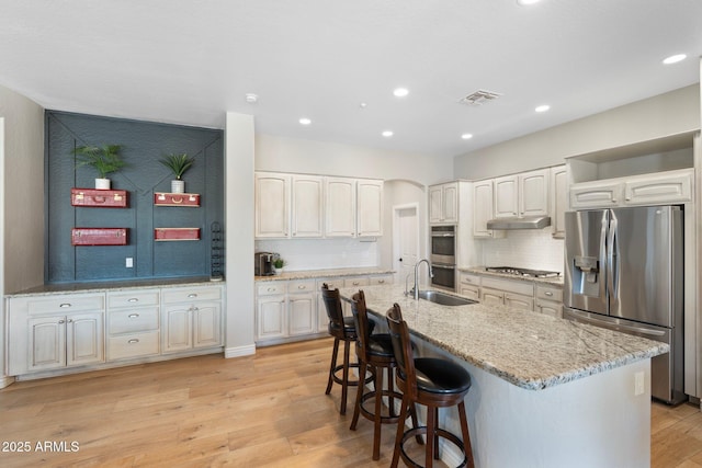 kitchen featuring stainless steel appliances, white cabinetry, a kitchen island with sink, and light hardwood / wood-style flooring