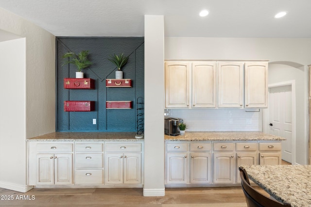 kitchen with light stone counters, decorative backsplash, cream cabinetry, and light wood-type flooring