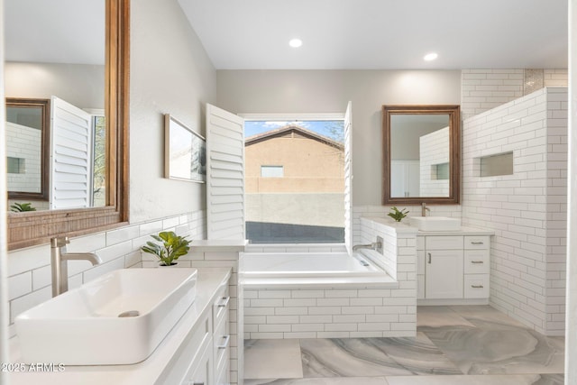 bathroom with tile walls, tiled tub, and vanity