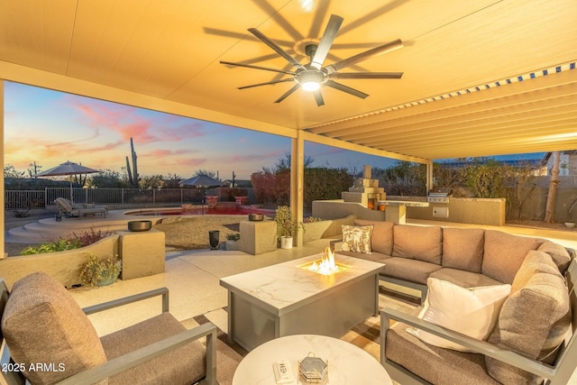 patio terrace at dusk featuring area for grilling, an outdoor living space with a fire pit, and ceiling fan