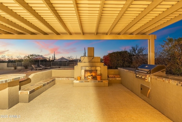 patio terrace at dusk with a tile fireplace, a grill, and area for grilling