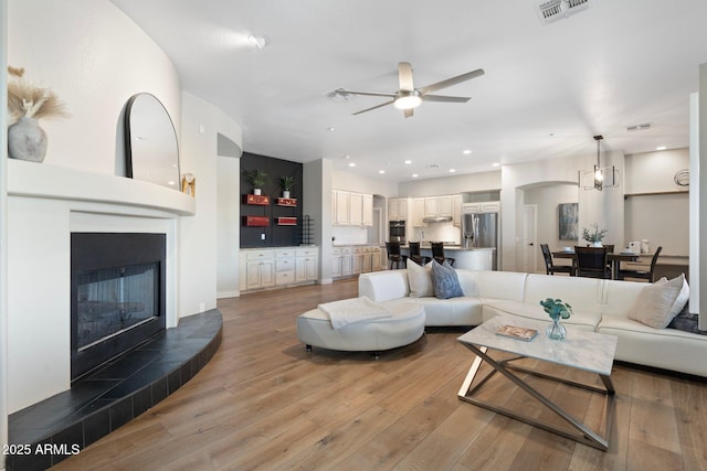 living room featuring a tiled fireplace, light hardwood / wood-style flooring, and ceiling fan