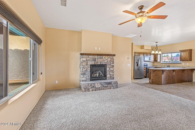 unfurnished living room with a stone fireplace, light carpet, sink, and ceiling fan with notable chandelier