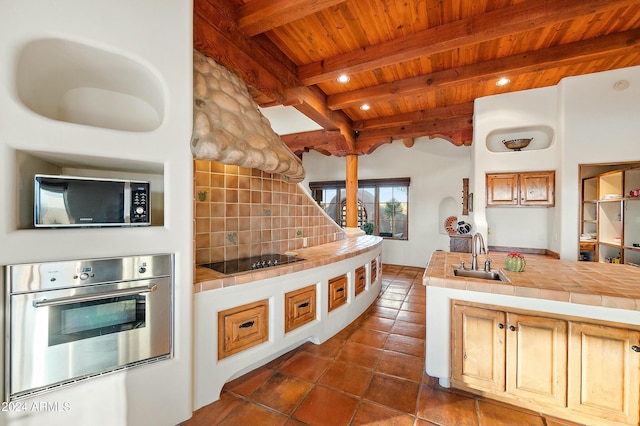 kitchen featuring beam ceiling, tile counters, stainless steel oven, and sink