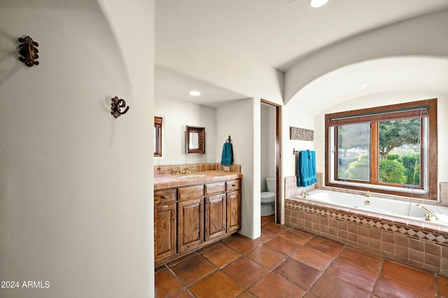 bathroom with tile patterned flooring, vanity, a relaxing tiled tub, and toilet