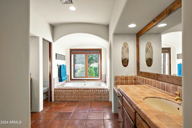 bathroom with vanity, a relaxing tiled tub, and toilet