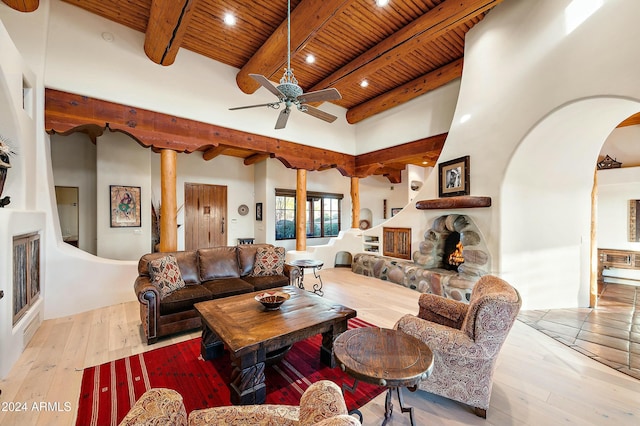 living room with beam ceiling, a stone fireplace, ceiling fan, and a high ceiling