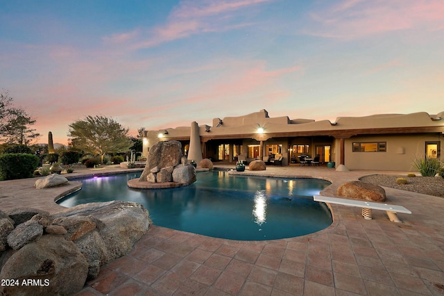 pool at dusk with a diving board and a patio area