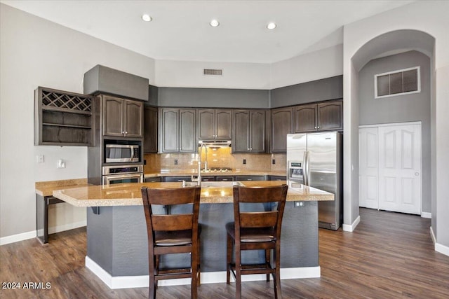 kitchen featuring a center island with sink, a kitchen breakfast bar, dark hardwood / wood-style floors, dark brown cabinetry, and stainless steel appliances