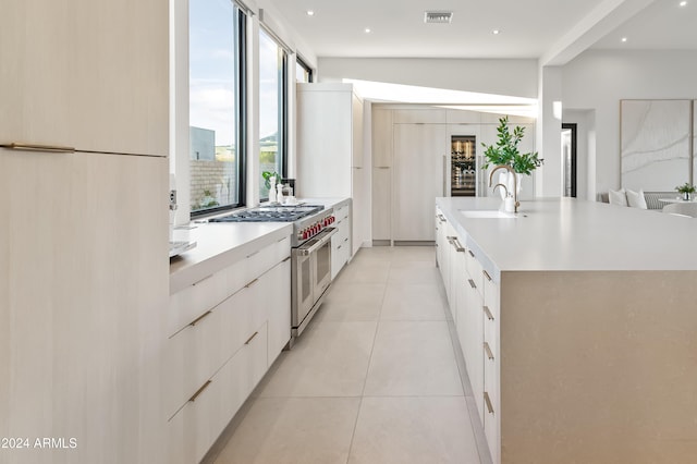 kitchen with an island with sink, white cabinetry, sink, double oven range, and white refrigerator