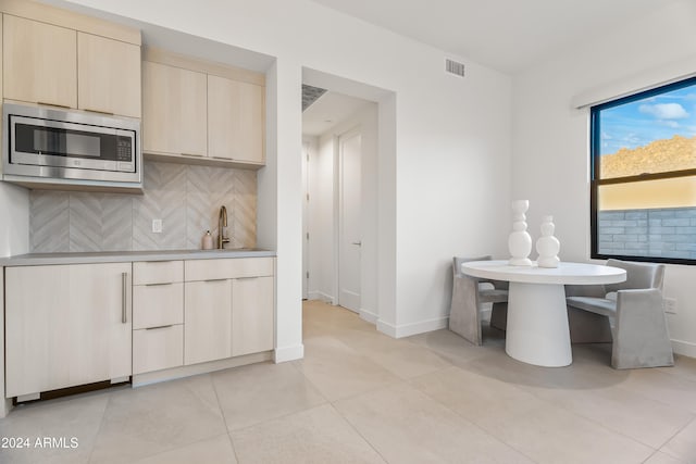 kitchen featuring sink, light tile patterned flooring, stainless steel microwave, and backsplash