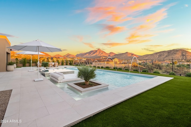 pool at dusk featuring a patio, a mountain view, pool water feature, and a lawn