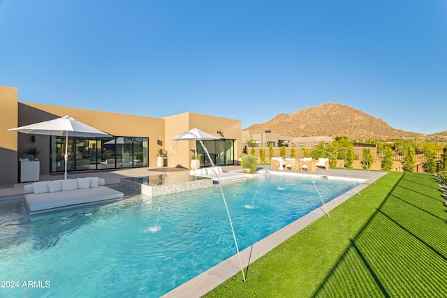 view of pool featuring pool water feature, a mountain view, a patio area, and a lawn