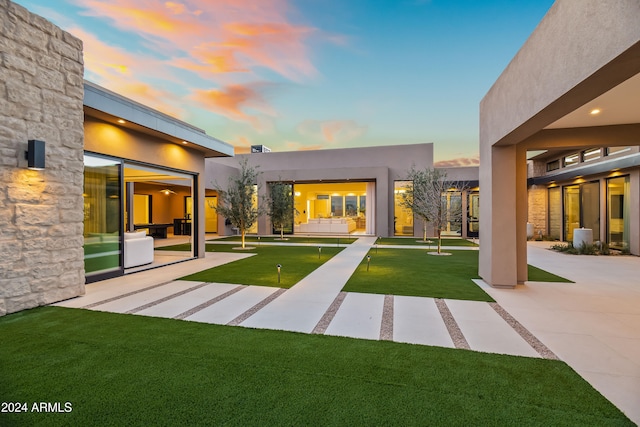 back house at dusk featuring a yard and a patio area