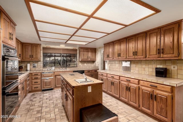 kitchen featuring tasteful backsplash, double wall oven, sink, and an island with sink