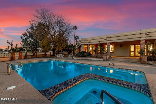 pool at dusk featuring an in ground hot tub and a patio area