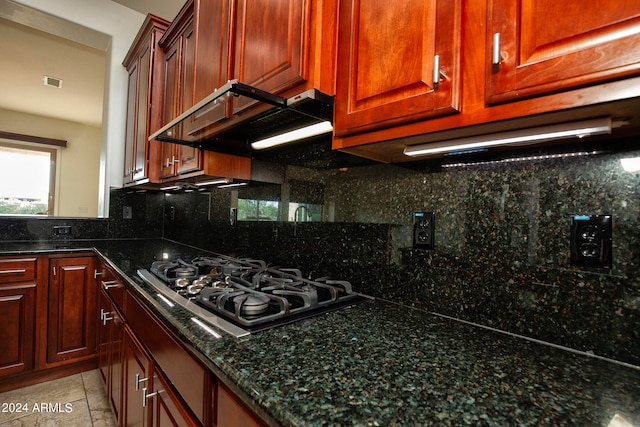 kitchen with tasteful backsplash, dark stone counters, range hood, light tile patterned floors, and stainless steel gas stovetop