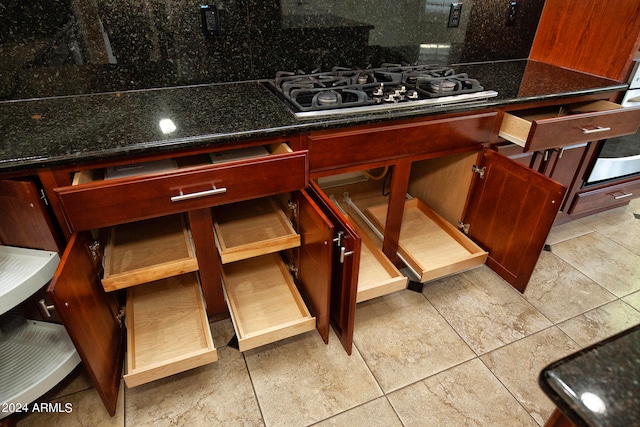 kitchen with dark stone counters, light tile patterned floors, stainless steel gas stovetop, and backsplash