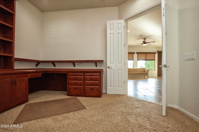 unfurnished office featuring light carpet, built in desk, and ceiling fan