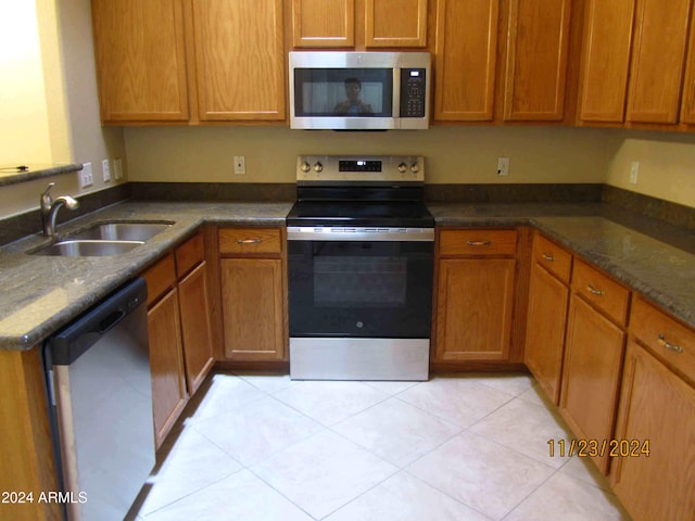 kitchen with dark stone countertops, sink, light tile patterned floors, and stainless steel appliances