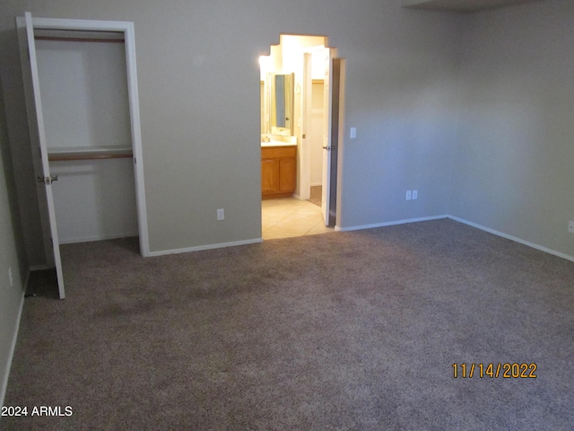 unfurnished bedroom with connected bathroom, light colored carpet, and a closet