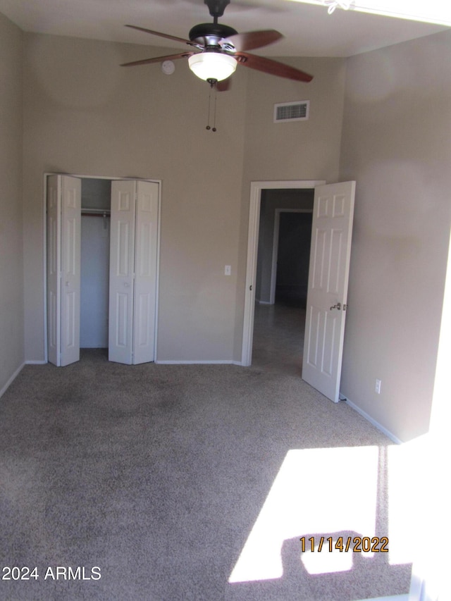 unfurnished bedroom featuring carpet, a high ceiling, a closet, and ceiling fan