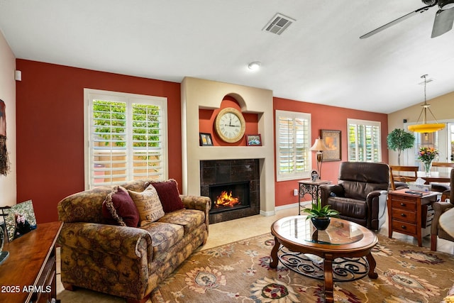 living room featuring ceiling fan, vaulted ceiling, a tile fireplace, and a healthy amount of sunlight