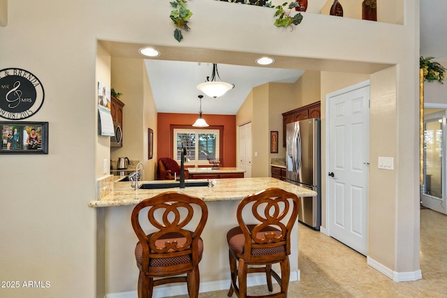 kitchen featuring pendant lighting, sink, a kitchen breakfast bar, stainless steel refrigerator with ice dispenser, and kitchen peninsula