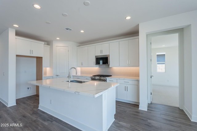 11857 N Luckenbach St, Surprise, AZ 85388 - kitchen featuring appliances with stainless steel finishes, a sink, a center island with sink, decorative backsplash, and dark wood-type flooring